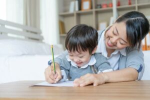 A smiling toddler learning how to write from a tutor