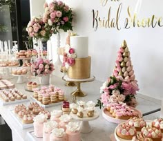 Elegant outdoor wedding dessert table with a pink-themed cake, cupcakes, and assorted sweets, decorated with flowers.